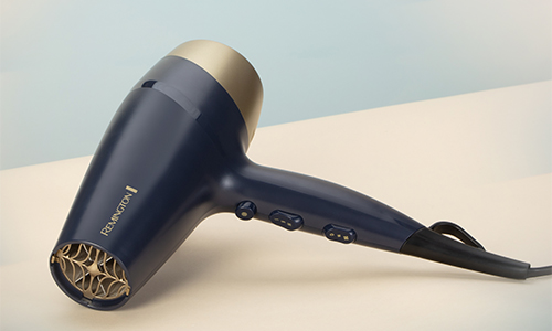 Asciugacapelli blu scuro e oro su una superficie bianca, con cavo nero. La marca "Remington" � visibile sul lato.