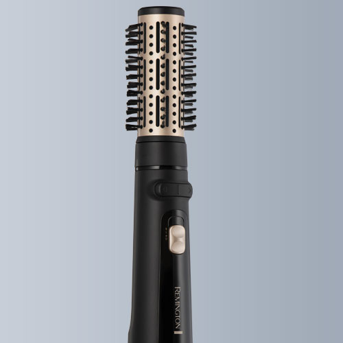 Spazzola ad aria calda Remington nera e dorata con setole cilindriche su sfondo grigio-blu.