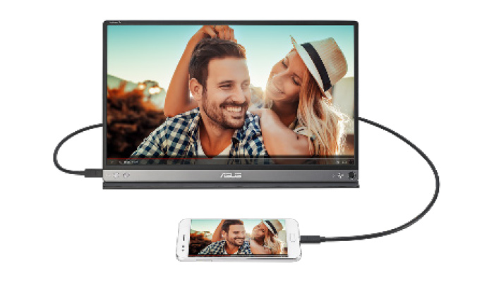 Monitor collegato a smartphone con cavo. Schermo mostra uomo e donna sorridenti in ambiente esterno luminoso.