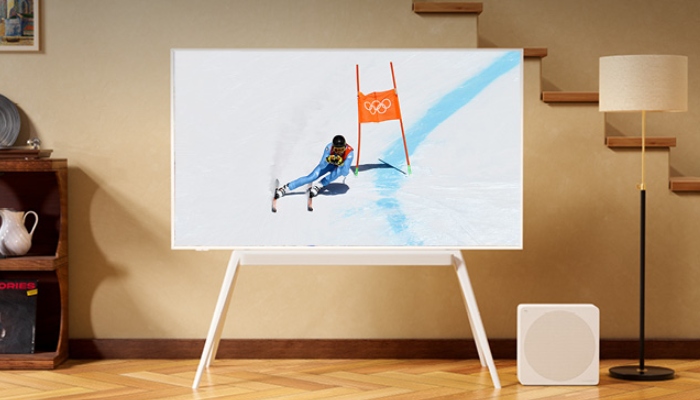 Si vede il salotto di una casa con delle scale in sottofondo e una tv in primo piano con un uomo che scia in modo professionale