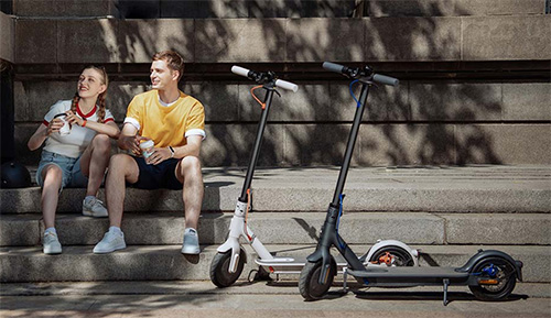 Uomo e donna seduti su scalini di pietra con due monopattini elettrici parcheggiati di fronte a loro.