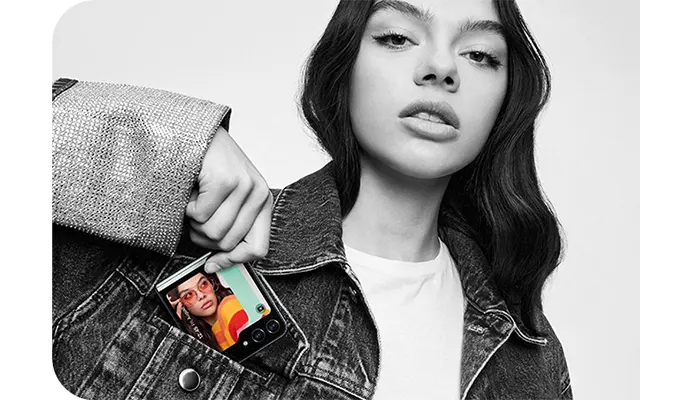 Una persona in giacca di jeans tiene un telefono in tasca che mostra un'altra persona. Lo sfondo � grigio.