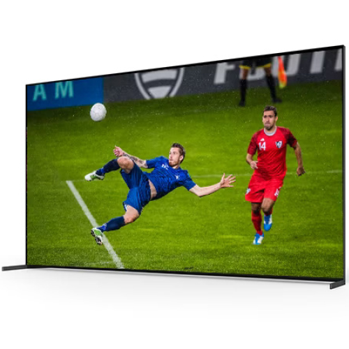 Schermo TV che mostra due calciatori in campo verde, uno in blu che calcia una palla bianca. Un altro giocatore in rosso corre.