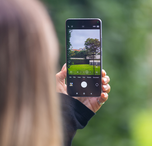 Persona tiene in mano un cellulare che mostra un prato verde con un albero e una casa bianca, su sfondo verde.