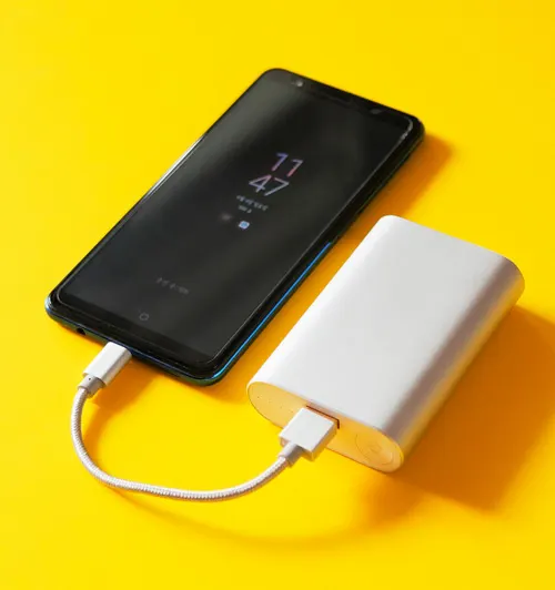 Su sfondo giallo, un telefono nero � collegato a una power bank bianca tramite un cavo. Sul display del telefono si legge l'ora 11:47.