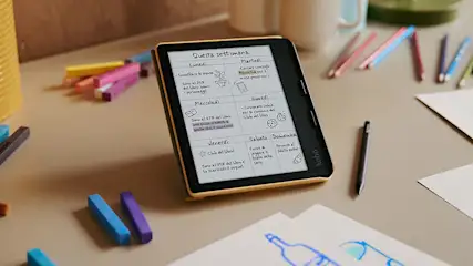 E-reader con agenda settimanale, pennarello e pastelli colorati su tavolo. Fogli con disegni sparsi.