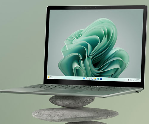 Un laptop aperto su pietre impilate. Lo schermo mostra un motivo astratto verde. Lo sfondo � verde chiaro.