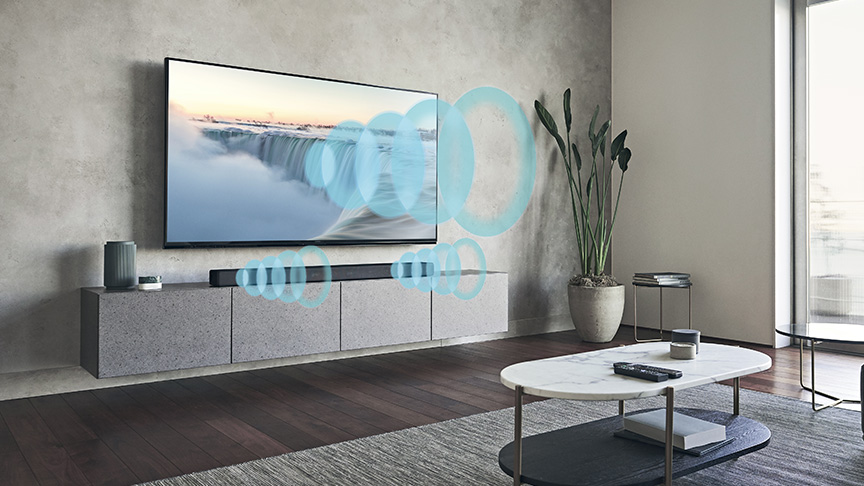 Soggiorno con TV che mostra cascata, soundbar e cerchi blu. Tavolino con telecomando su tappeto grigio. Pianta decorativa in vaso.