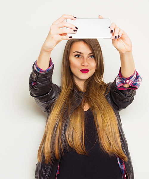 Donna che scatta una foto con un telefono cellulare. Indossa una giacca di pelle nera su una camicia nera e una camicia a quadri.