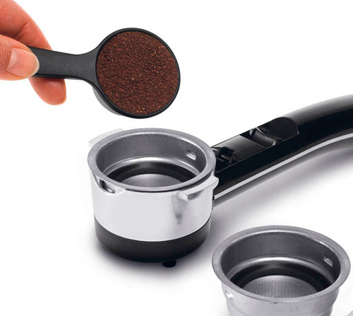 Mano con misurino versa caff� macinato in filtro porta per macchina espresso nera e argento su sfondo bianco.