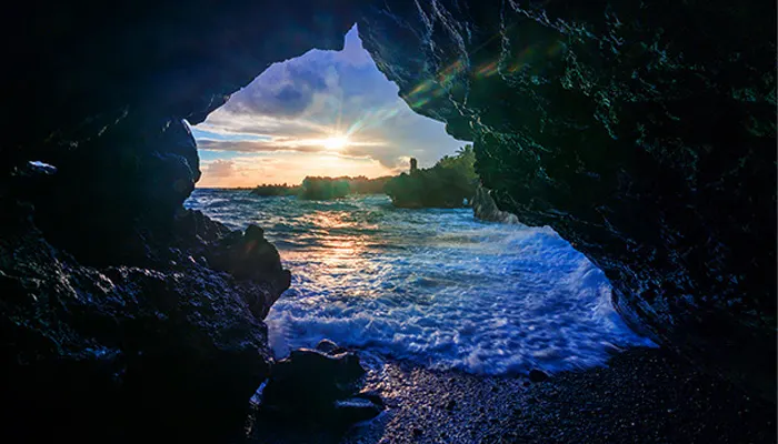 Un paesaggio all'interno di una grotta dalla quale si puo' vedere il mare e il sole nel cielo