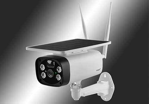 Telecamera di sicurezza bianca con pannello solare e antenne su supporto a muro. Lo sfondo è grigio sfumato.