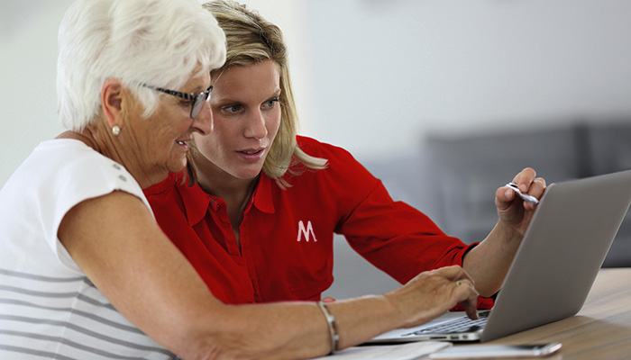 Due donne guardano un portatile. Una donna in rosso indica lo schermo, l'altra tocca la tastiera.