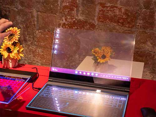 Un tavolo rosso con un laptop trasparente che mostra una schermata con girasoli e un'altra schermata colorata.