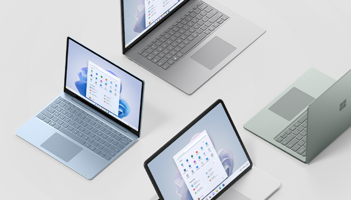 Disposizione di laptop grigi e un tablet con Windows su uno sfondo bianco, che mostra schermi e tastiere.