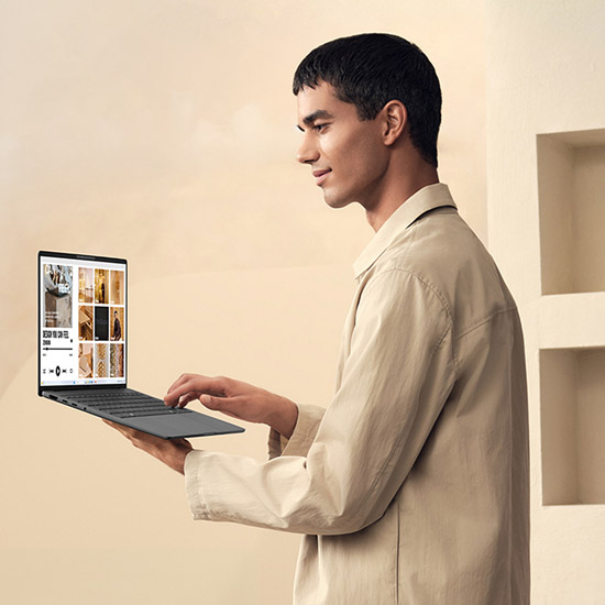 Un uomo in camicia beige usa un laptop nero. Lo schermo del laptop mostra varie immagini. Lo sfondo è beige chiaro.