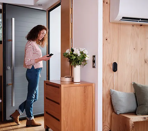 Donna in jeans e maglietta a righe guarda il telefono vicino alla porta. Com� in legno con fiori e aria condizionata.