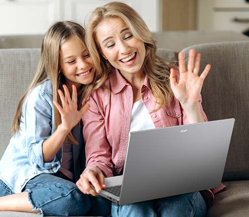 Madre e figlia sedute su un divano grigio salutano con la mano ad un laptop grigio.