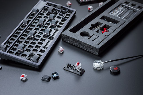 Tastiera meccanica smontata con accessori: interruttori, cappucci, pennello per lubrificante, scatola portaoggetti su sfondo scuro.