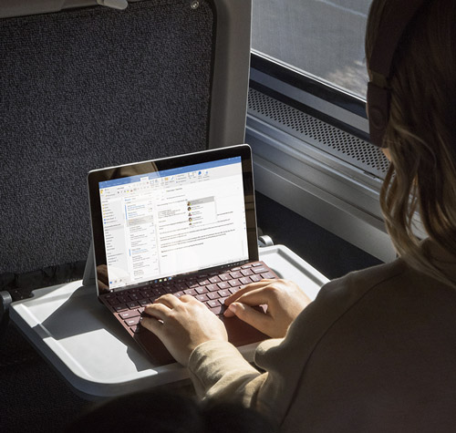 Donna usa un laptop su un tavolino in treno, con una finestra sullo sfondo.