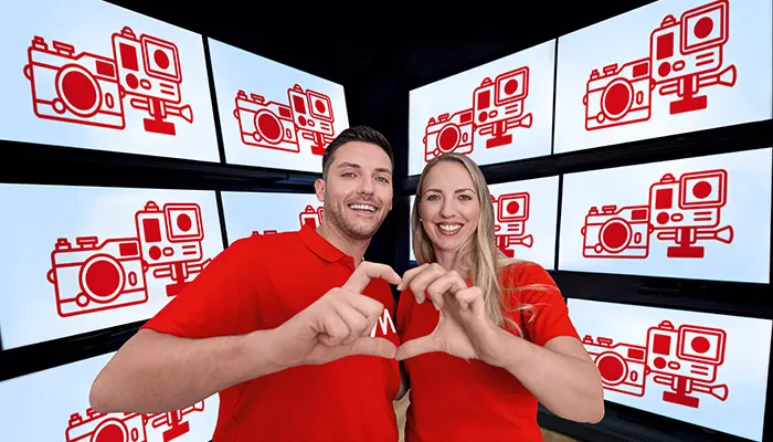 Uomo e donna sorridono, mani a forma di cuore, sfondo con schermi e icone di fotocamere rosse.
