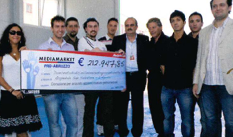 Dieci persone posano con un assegno blu e bianco di MediaMarket per PRO-ABRUZZO, per 212.947,86 euro.