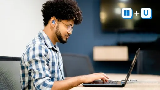 uomo in un ufficio sta seduto davanti al suo portatile. Indossa un apparecchio acustico