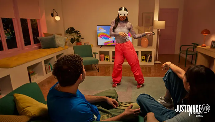 Una donna con visore VR balla in salotto, mentre due persone la guardano sedute su un divano.