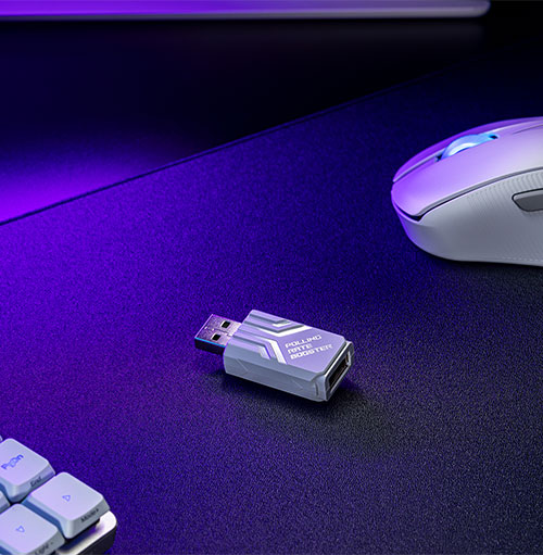 Su una scrivania viola scuro sono presenti una tastiera bianca, un mouse bianco e una chiavetta USB grigia.