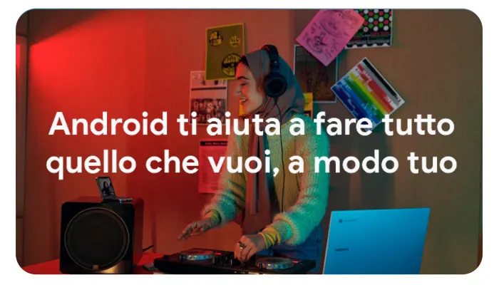 Una persona con cuffie mixa musica su un giradischi, con laptop blu e speaker neri vicini. Muro con poster colorati sullo sfondo.