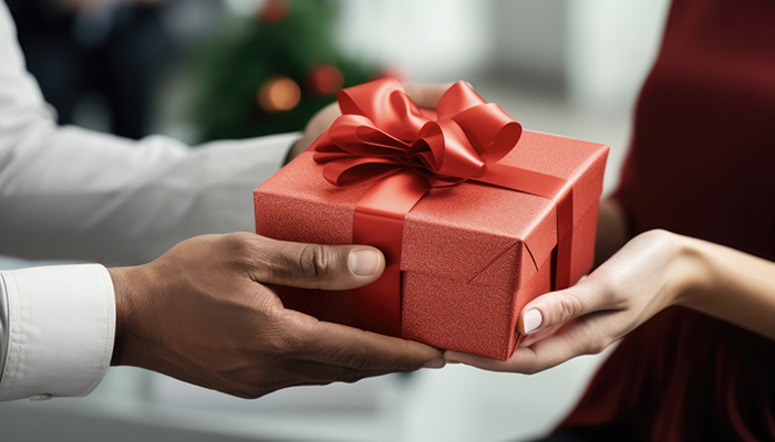 Uomo che offre un regalo rosso con nastro a donna. Albero decorato sullo sfondo.