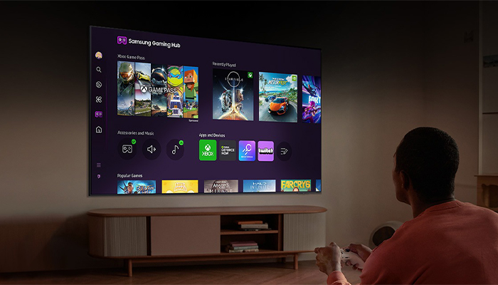 Un uomo guarda una TV che mostra il Samsung Gaming Hub con diverse icone di giochi e applicazioni.