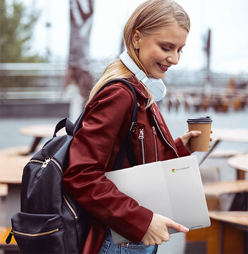 Donna sorridente con giacca rossa, zaino nero, cuffie bianche, laptop e caff�. Tavoli sullo sfondo.