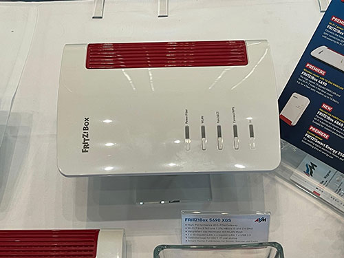 Un router bianco "Fritz!Box" con dettagli rossi su un tavolo, con indicatori neri e un depliant blu sullo sfondo.