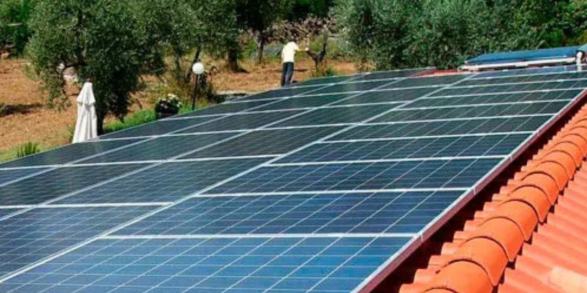 Pannelli solari su un tetto di tegole rosse, con una persona in piedi sopra e alberi sullo sfondo.