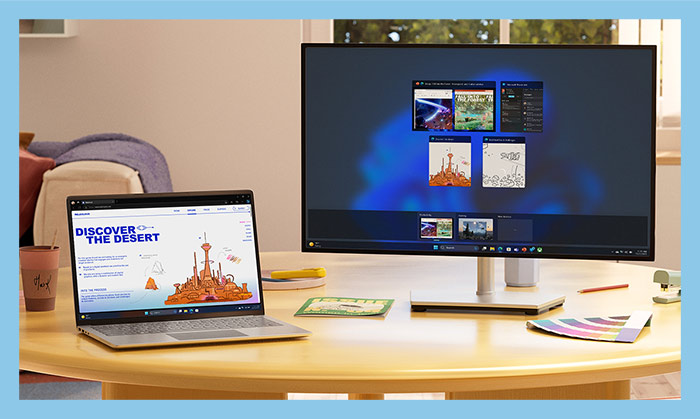 C'� un laptop aperto con la scritta "Discover the desert" e un monitor con finestre aperte su un tavolo di legno.