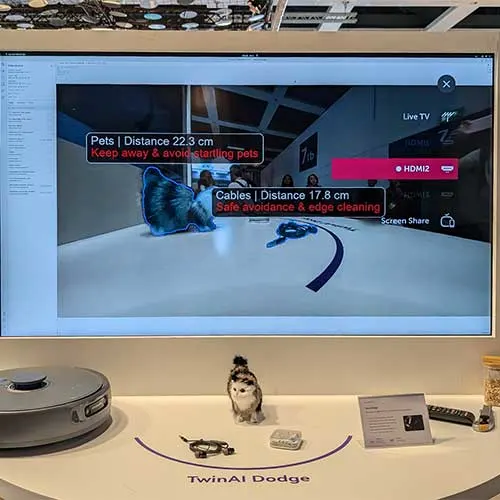 Schermo TV che mostra un robot aspirapolvere che evita ostacoli come animali domestici e cavi. Robot aspirapolvere in basso a sinistra.
