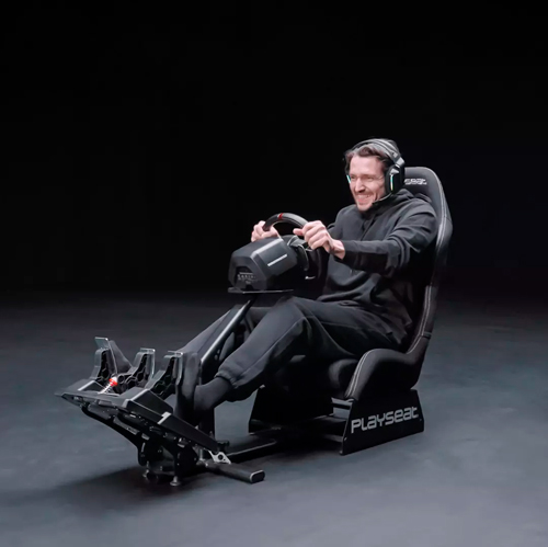 Un uomo seduto su una sedia da gioco nera con cuffie, che tiene un volante con i pedali per il simulatore.