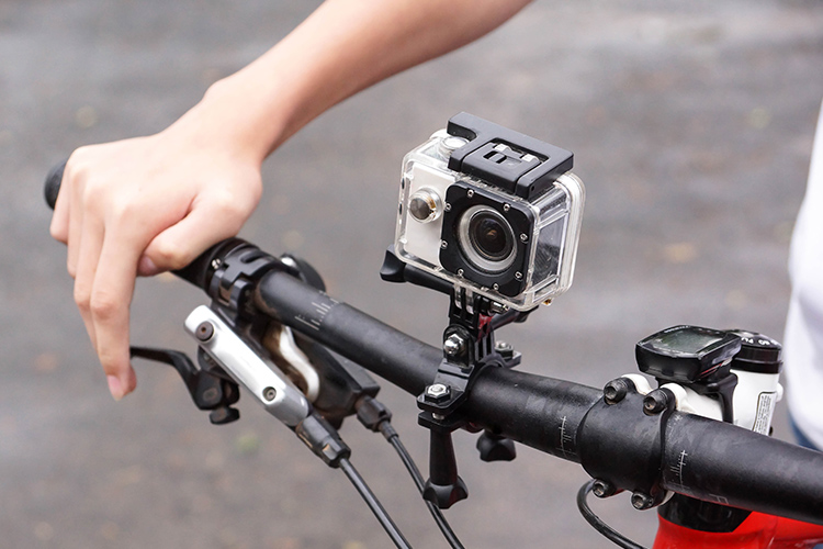 Una mano su un manubrio nero di bicicletta. Una action camera trasparente � montata sul manubrio. Visibile anche un ciclocomputer.