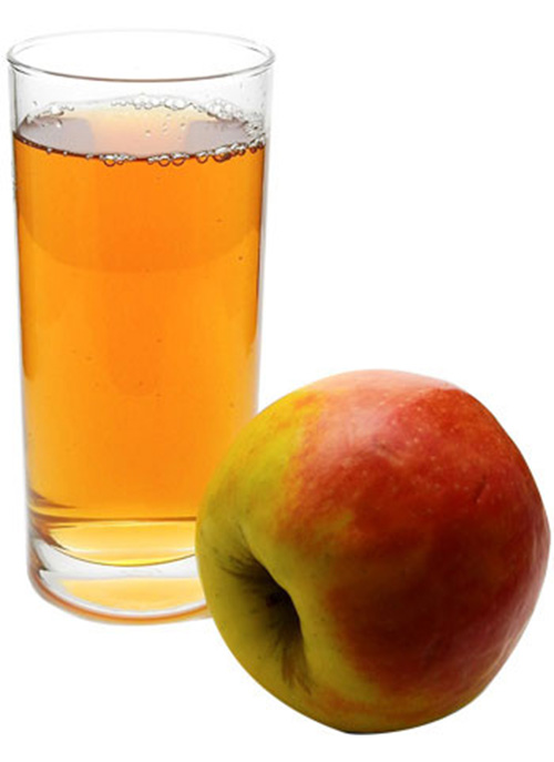 Su sfondo bianco, un bicchiere pieno di succo di mela color ambrato affiancato da una mela rossa e gialla.