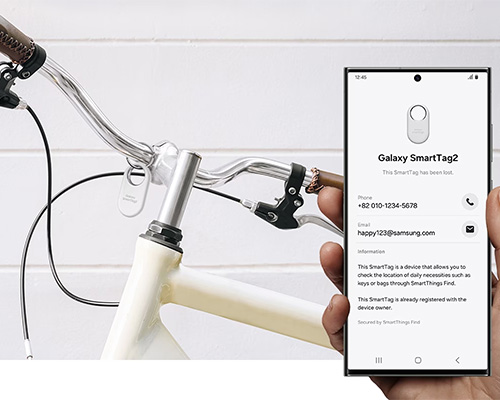 Bicicletta bianca con manubrio argento e telefono che mostra l'app Galaxy SmartTag2 per il tracciamento degli oggetti.