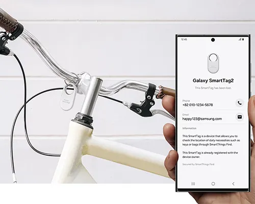 Bicicletta bianca con manubrio argento e telefono che mostra l'app Galaxy SmartTag2 per il tracciamento degli oggetti.