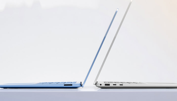 Due laptop aperti affiancati su una superficie bianca. Uno è blu e l'altro è argento. Entrambi mostrano le tastiere.