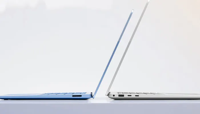 Due laptop aperti affiancati su una superficie bianca. Uno è blu e l'altro è argento. Entrambi mostrano le tastiere.