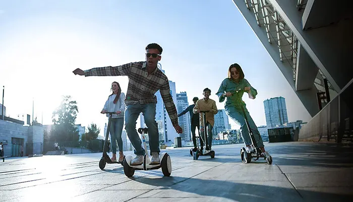 Un gruppo di persone su scooter elettrici su una superficie pavimentata con edifici sullo sfondo.