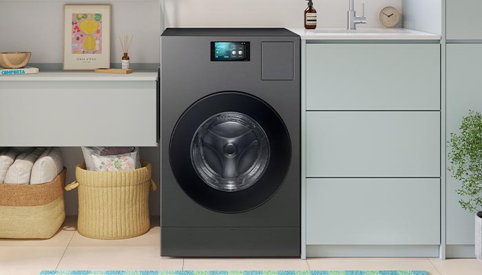 Lavatrice grigia accanto a mobili con cassetti in una stanza. Cesti di vimini sotto un ripiano con decorazioni.