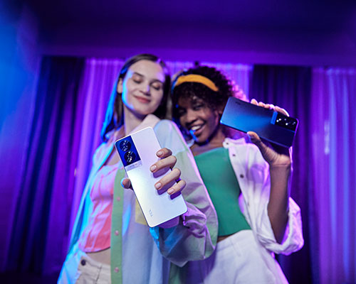 Due donne tengono in mano degli smartphone. Tende blu e viola sullo sfondo.