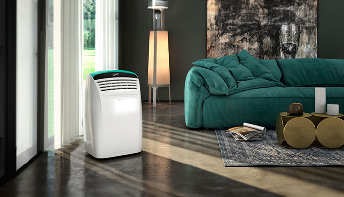 Soggiorno con condizionatore bianco, divano verde, tavolini dorati e tappeto decorato su pavimento lucido. Lampada alta e finestra.