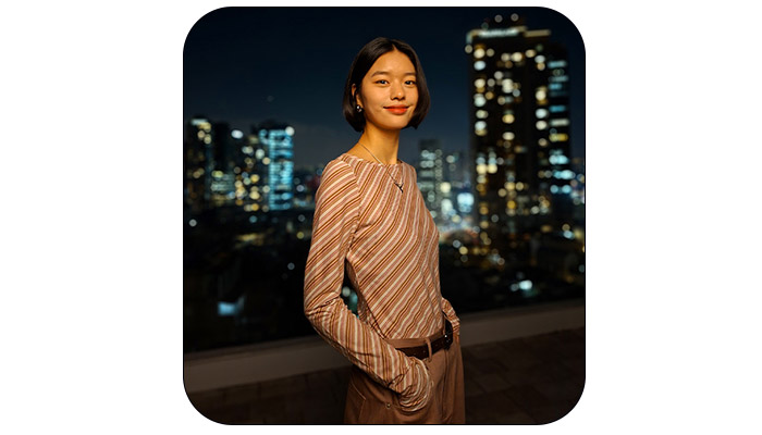 Una persona indossa una maglia a righe con pantaloni e cintura. Dietro, un paesaggio urbano notturno con edifici illuminati.