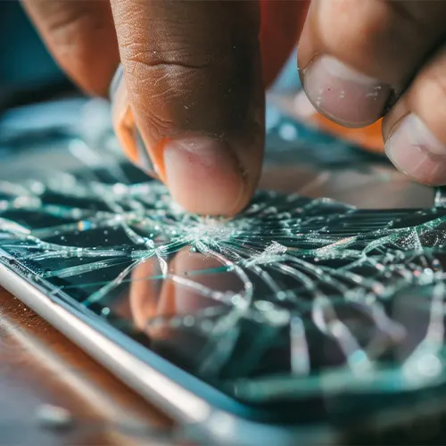 Dita che premono su uno schermo di cellulare rotto. Il vetro è crepato con riflessi di luce.